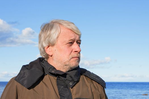 Portrait of mature concerned man with grey hair at the Baltic sea in autumn day.