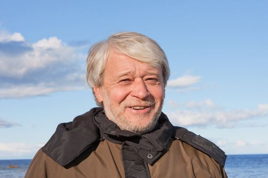 Portrait of mature smiling man with grey hair at the Baltic sea in autumn day.