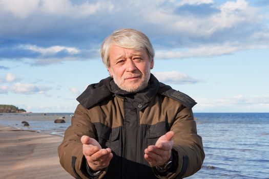 Mature poor man with grey hair at the Baltic sea asks for help in autumn day.