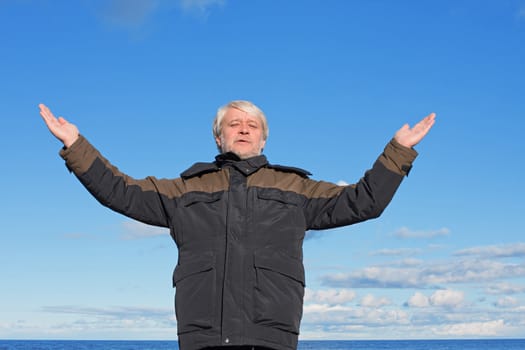 Mature man with grey hair relaxing at the Baltic sea and blue sky on the background.