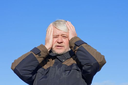 Portrait of mature desperate man with grey hair on blue sky of the background.