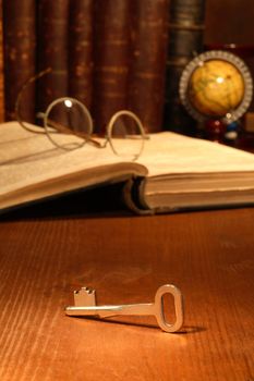 Old key lying on wooden background with books and spectacles