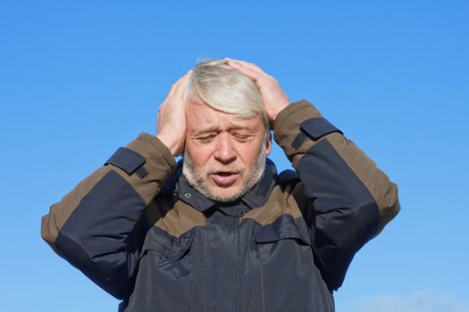 Portrait of mature desperate man with grey hair on blue sky of the background.