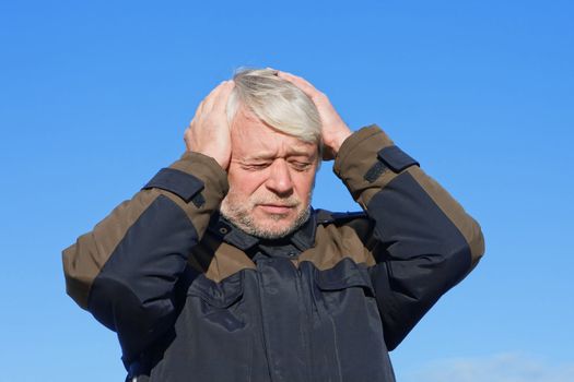 Portrait of mature concerned man with grey hair on blue sky of the background.