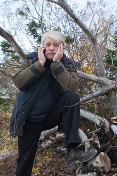 Mature busy man with grey hair in forest talking on the phone in autumn day.