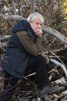 Mature serious man with grey hair in forest in autumn day.