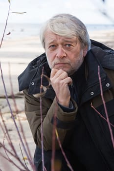 Portrait of mature serious man with grey hair at the Baltic sea in autumn day.