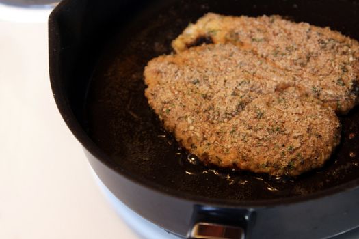Two pieces of breaded chicken frying in a frying pan.