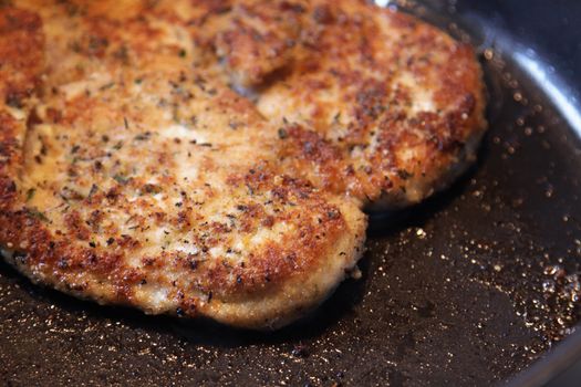 A close-up of breaded chicken frying in a frying pan.
