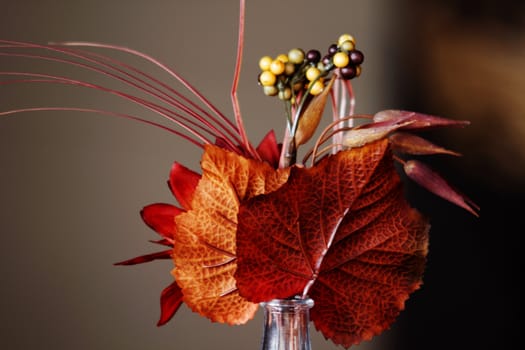Auburn and orange leaves with berries in a small, tabletop vase capture the beauty of the season 