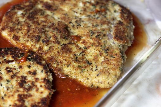 Breaded chicken sitting in a baking pan with tomato sauce.