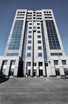 Dramatic black and white high rise office building tower with just a little blue color in the sky. The dark gloomy world of business and finance.