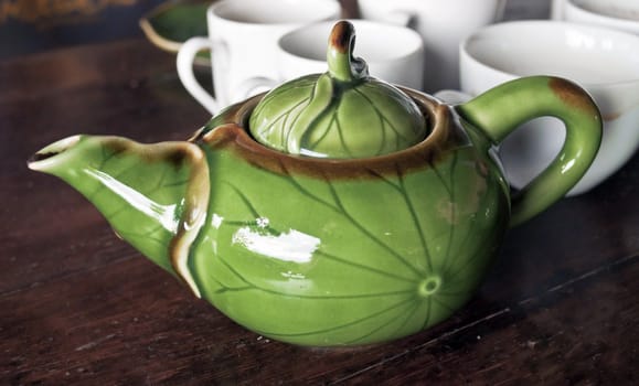 Greeb teapot with white cups in background on a wooden table