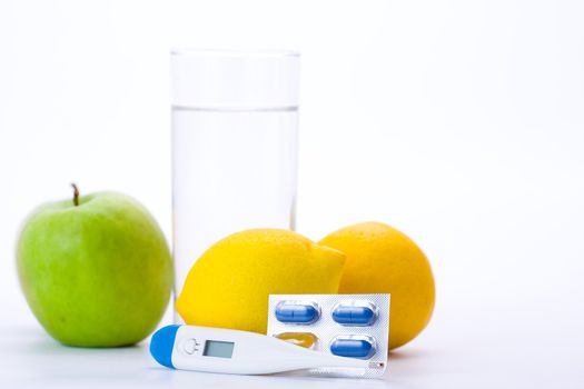 Thermometer, apple, water, lemons and pills representing illness.