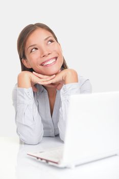 Woman thinking happy looking up at copy space while sitting at desk in front of laptop.