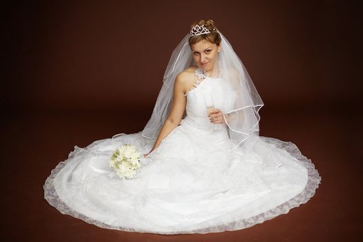 Young bride in a white dress sitting on a brown background