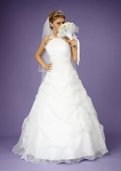 Young bride in a white dress with a bouquet on purple background