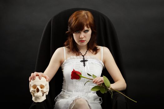 Young beautiful girl sitting in a chair with a skull and rose