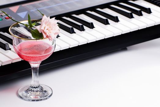 An electronic keyboard along with a fresh rose and a glass of pink wine, shot on white