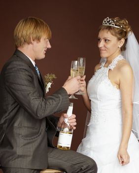 Newlywed couple drinking champagne clinking glasses on brown background