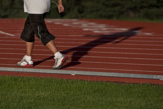 legs and full body shadow of female walker on red running tracks, focus on feet, motion blur