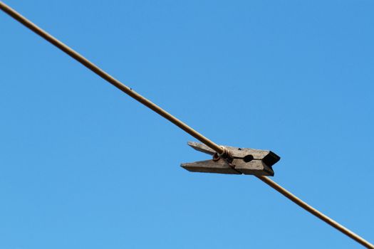 Single old and rusted cloths pin on a line against a cloudless blue sky