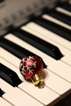 A red snowflake Christmas bauble sitting on piano keys.
