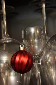 A red Christmas bauble ornament hanging from a dessert glass with wine glasses in the background.
