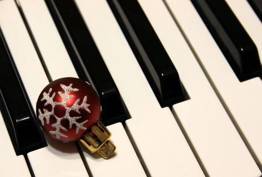 A red snowflake Christmas bauble sitting on piano keys.

