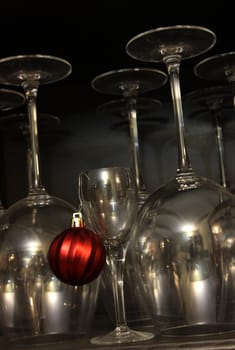 A red Christmas bauble ornament hanging from a dessert glass with wine glasses in the background.
