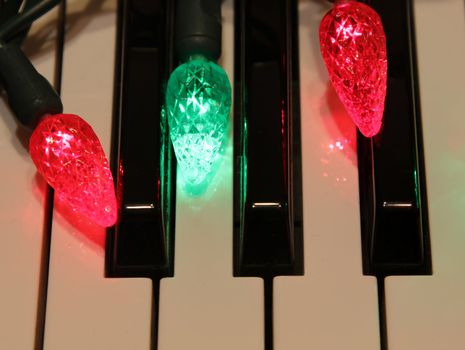 Red and green Christmas lights on piano keys.
