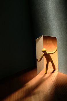 Yellow plasticine man entering to dark room. Conceptual composition with open door made from paper