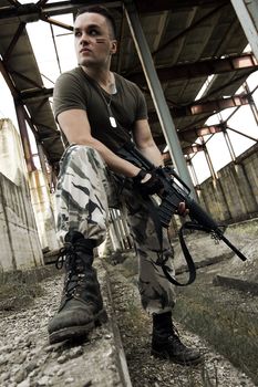 Man in camouflage with pneumatic gun over ruins