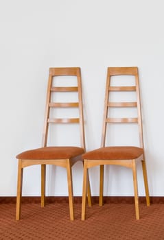 Two modern wooden chair. White wall and brown floor