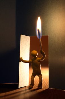 Yellow plasticine man with lighting match entering to dark room. Conceptual composition with open door made from paper