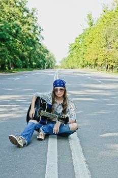 Rocking girl on a highway road with guitar