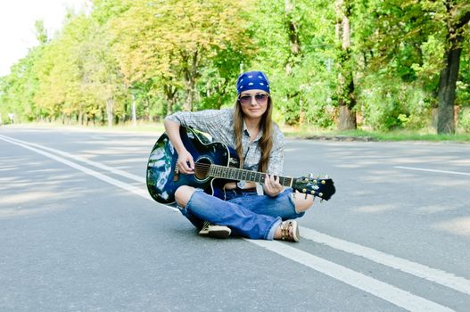 Rocking girl on a highway road with guitar