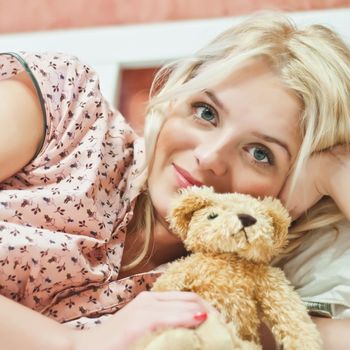 Beautiful young girl with bear toy in bed