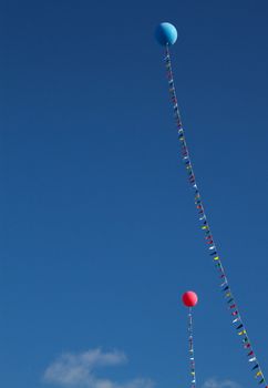 Two  helium balloons, one red and one blue, held in place by a flagged line against a blue sky