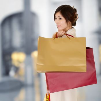 Modern woman shopping in mall holding bags and thinking.