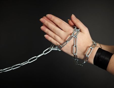 Women's hands shackled a metal chain on a dark background