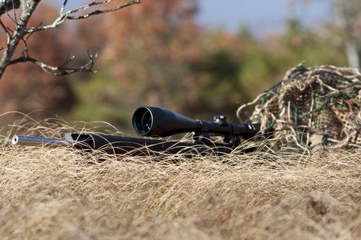 sniper laying on the ground covered in a ghille suite tall grass and trees in the background