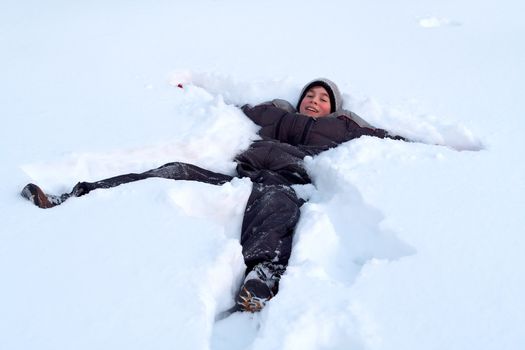 A happy young boy lays in fresh snow as he plays outdoors on a cold winter day.