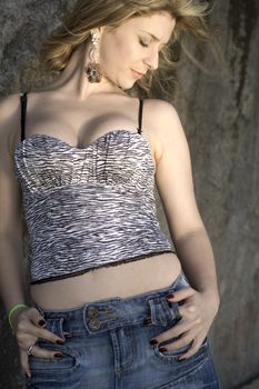 A very pretty and young blond brazilian woman wearing a black and white, zebra like top and jeans skirt next to rocks.