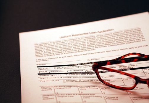 Home loan application against black background. Financial document for mortgage loan with a pair of glasses in the foreground.