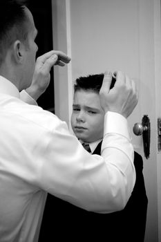 A groom helps his son get ready by doing his hair.