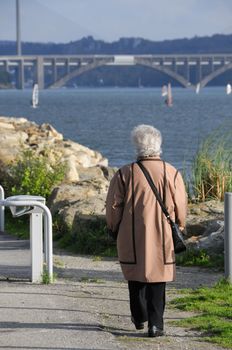 Senior woman walking along the coast in Le Relecq Kerhuon with the bridges "Pont Plougastel" and "Pont de l'Iroise" in the background.