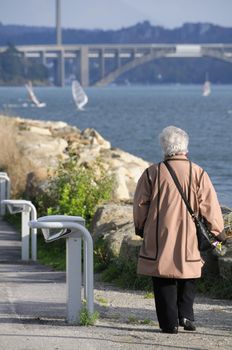 Senior woman walking along the coast in Le Relecq Kerhuon with the bridges "Pont Plougastel" and "Pont de l'Iroise" in the background.