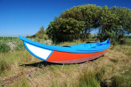 Colorful fishing boat on green grass on a sunny day with clear blue sky.