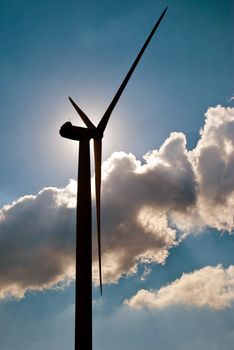 Wind turbine in the back light of the sun with blue sky and clouds.